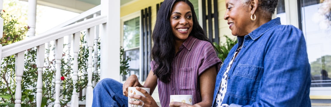 Mother and adult daughter talking on a front porch, symbolizing open conversations about passing on a family home to the next generation.